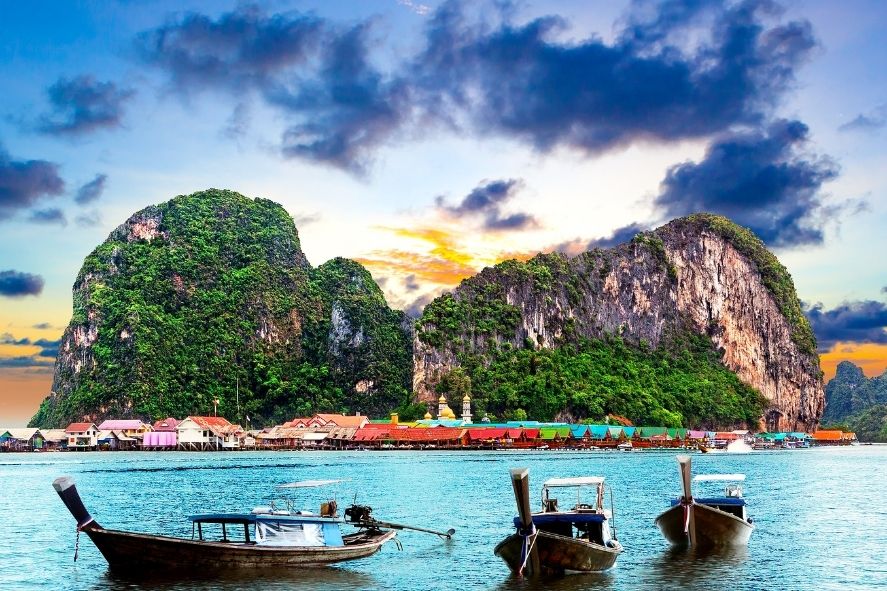 boats by limestone cliffs in phuket at sunset